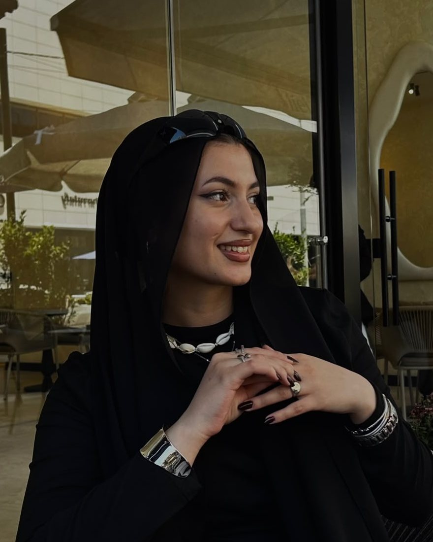 Portrait of Lian Altamimi, smiling, in a black hijab at a café in Amman